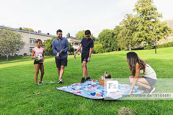 Woman laying out picnic blanket with family on grass in lawn
