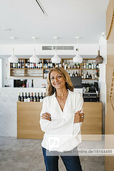 Happy businesswoman with arms crossed standing at restaurant