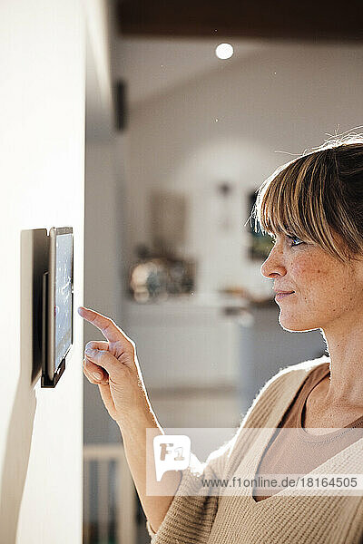 Woman touching tablet PC mounted on wall at home
