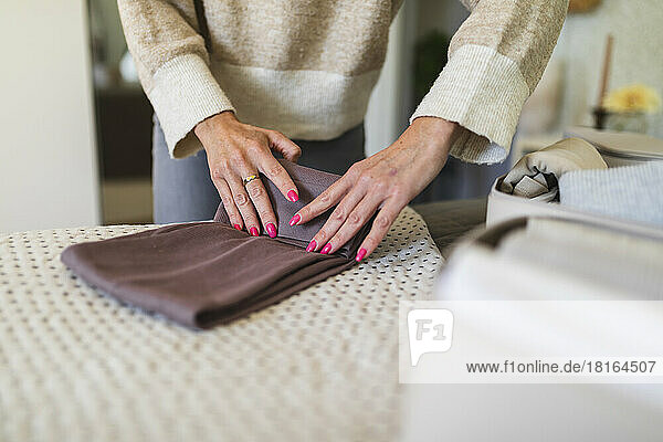 Hands of mature woman folding clothes on bed