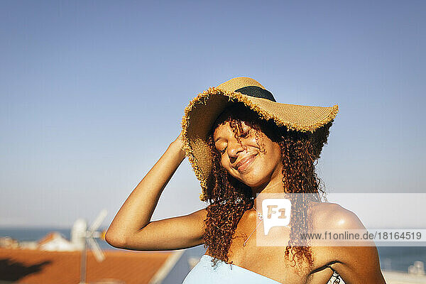 Lächelnde Frau mit geschlossenen Augen und Hut an einem sonnigen Tag