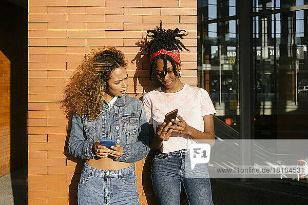 Young woman showing mobile phone to friend on sunny day