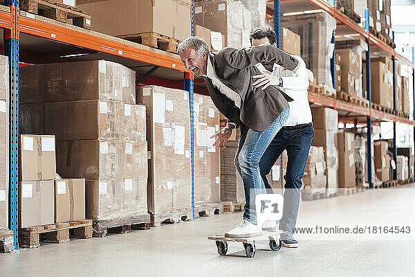 Happy businessman skateboarding with colleague at warehouse