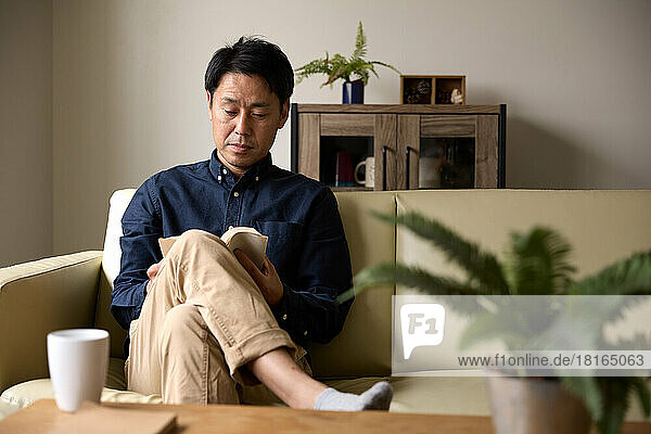 Japanischer Mann liest ein Buch auf dem Sofa