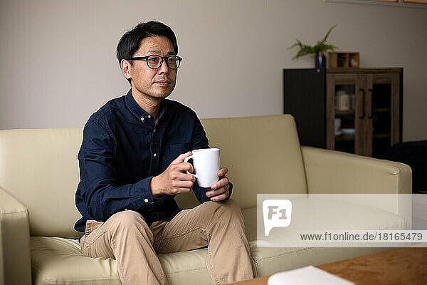 Japanese man relaxing on the sofa with beverage in hand