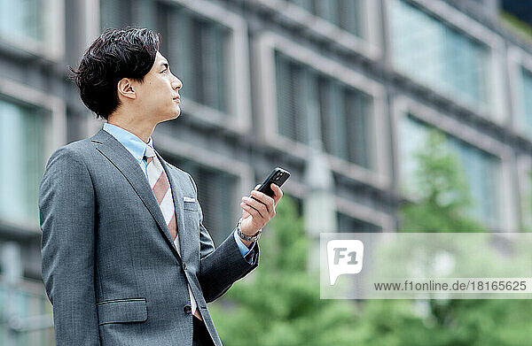 Japanischer Geschäftsmann hält ein Smartphone und schaut weg