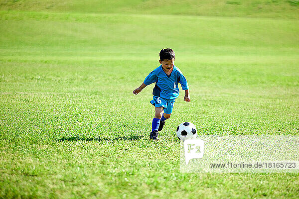 Japanisches Kind spielt Fußball in einem Stadtpark