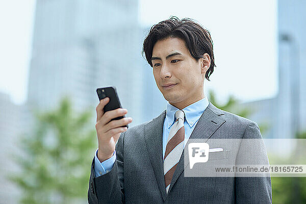 Japanischer Geschäftsmann mit Blick auf ein Smartphone