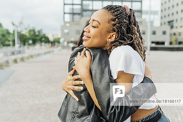 Young woman hugging friend on footpath