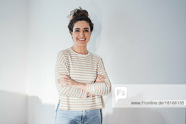 Happy woman with arms crossed leaning on white wall at home