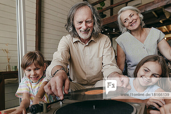Smiling grandfather changing record on turntable by granddaughters at home