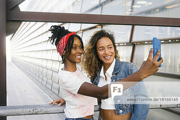 Smiling multiracial women taking selfie on mobile phone by railing