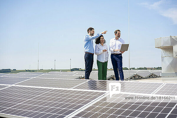Businessman gesturing to colleagues discussing by solar panels on rooftop