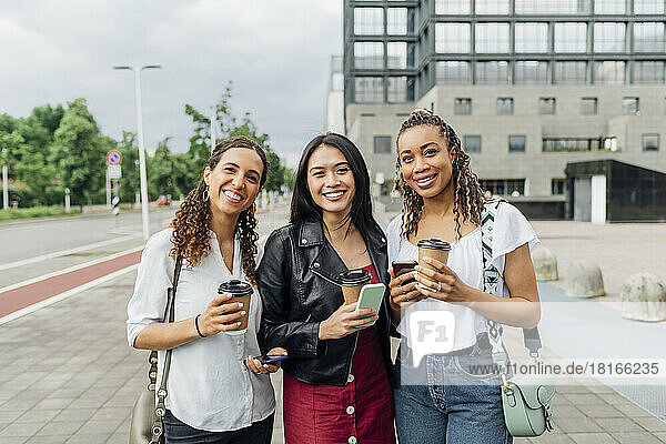 Smiling multiracial friends with reusable coffee cups standing on footpath