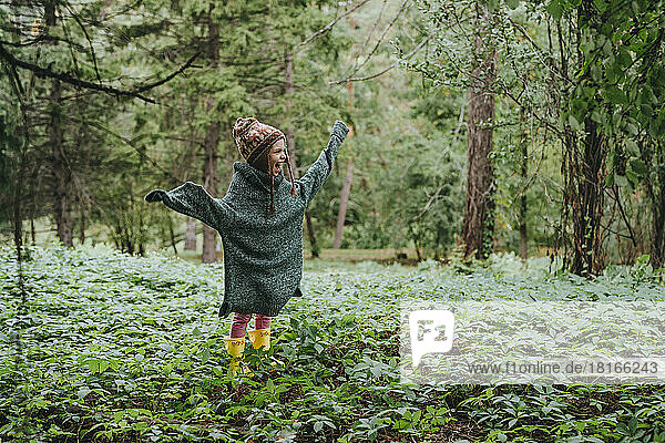 Happy girl in oversized sweater standing amidst forest