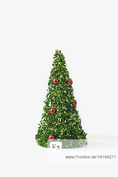 Small christmas tree made of green confetti and red baubles against white background