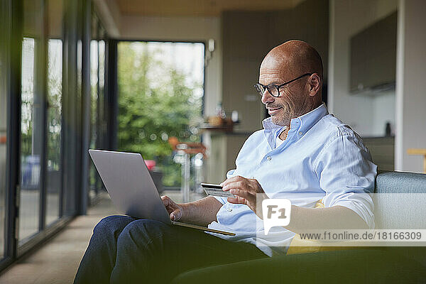 Lächelnder älterer Mann  der zu Hause mit Kreditkarte am Laptop bezahlt