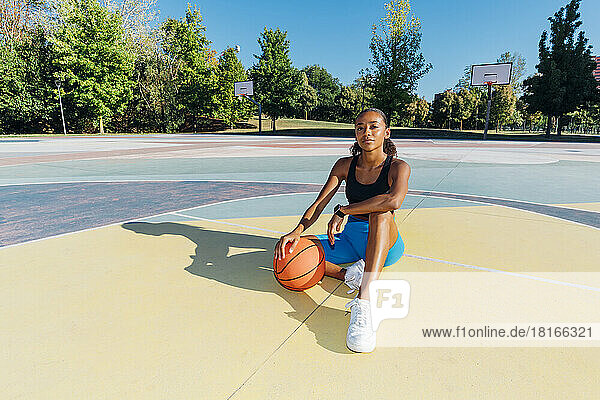 Confident sportswoman with basketball sitting on court