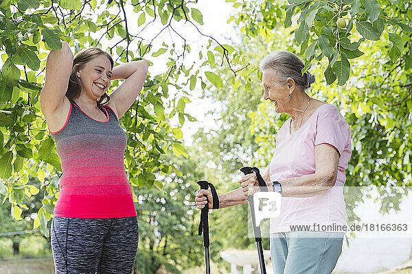 Happy fitness instructor with senior woman standing by tree