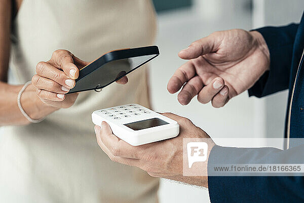 Hand of salesman holding credit card reader with woman paying