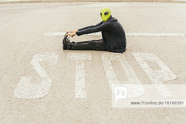 Mann mit Alienmaske sitzt vor STOP-Schild auf der Straße