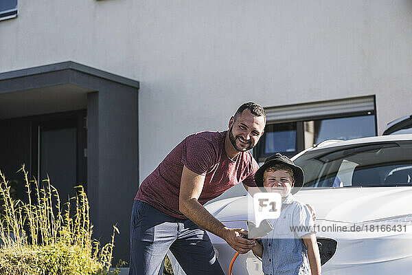 Father and son charging electric car in front of residential house