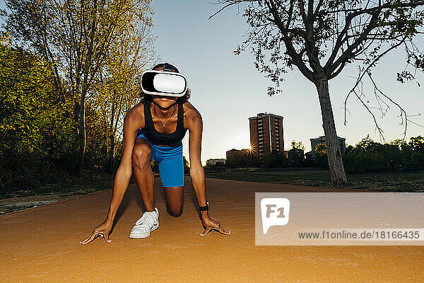Junge Sportlerin mit VR-Brille kniet auf Fußweg im Park