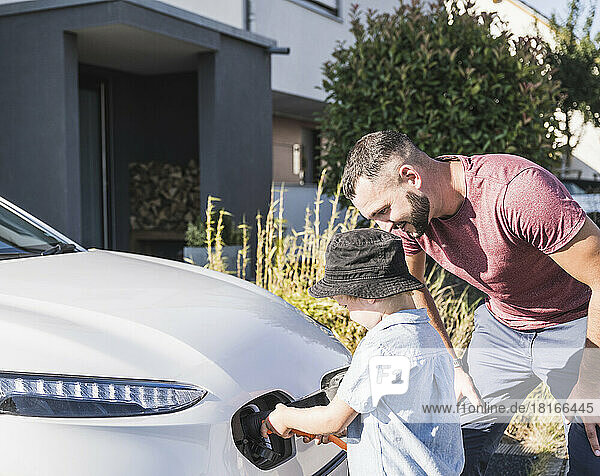 Father and son charging electric car in front of residential house