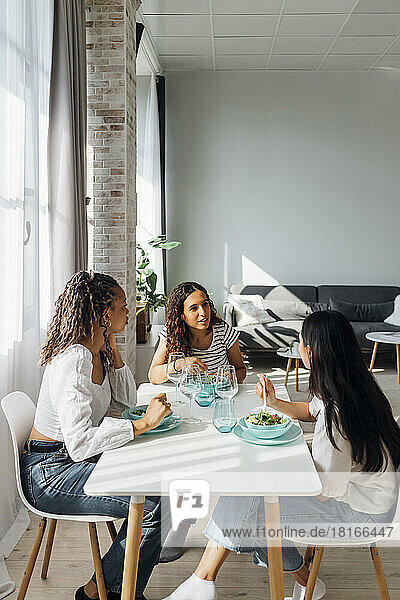 Junge Freunde reden und essen Salat am Esstisch im Wohnzimmer