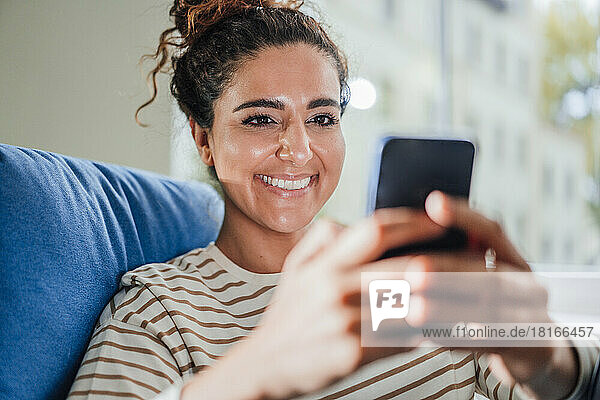 Smiling woman text messaging on mobile phone at home