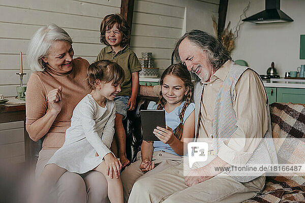 Happy grandparents with kids watching tablet PC at home