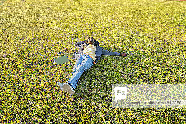 Businessman with mobile phone and laptop resting on grass
