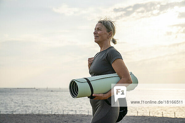 Mature woman holding exercise mat at sunset