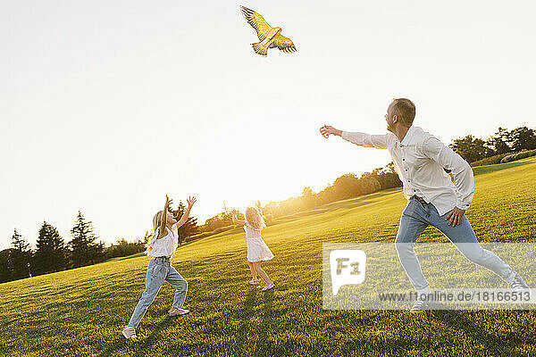 Daughters having fun with father flying kite in park