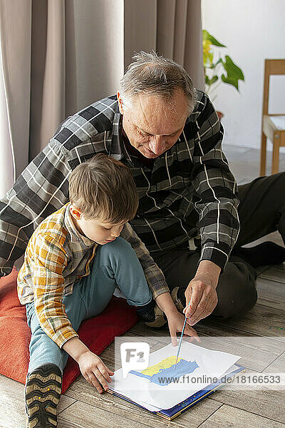 Grandfather with grandson drawing Ukrainian flag on paper at home