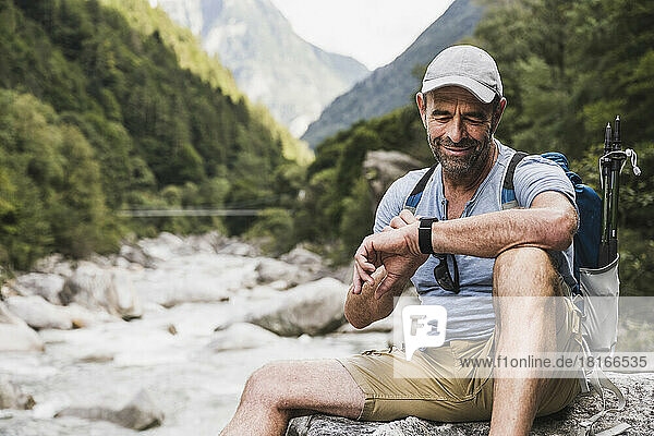 Smiling man checking time on wristwatch sitting in front of mountains