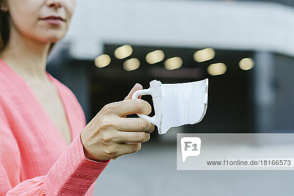 Hand einer Frau  die eine zerbrochene Kaffeetasse hält