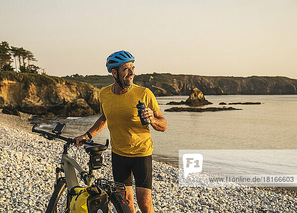 Happy man with bicycle holding water bottle at beach