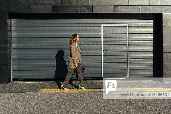 Young businesswoman walking on street by corrugated wall