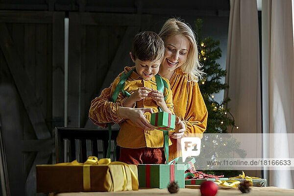 Boy helping mother in wrapping Christmas gifts at home
