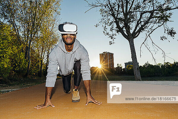 Sportsman wearing VR Goggles kneeling at starting line in park
