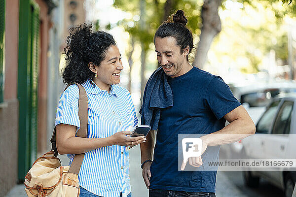 Lächelnde Frau teilt Smartphone mit Freund auf Fußweg