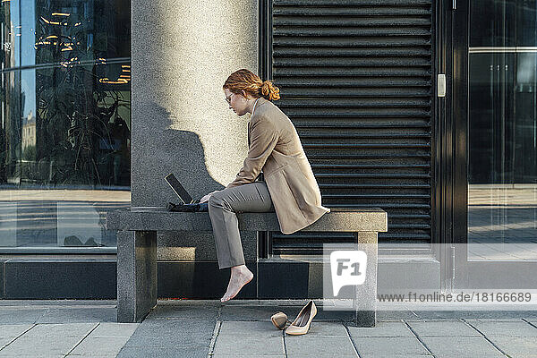 Young redhead freelancer using laptop by office building