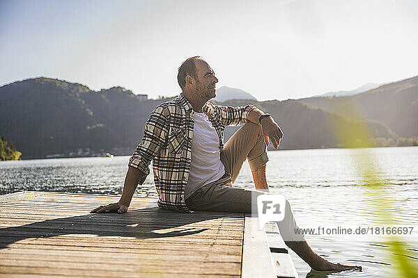 Thoughtful man sitting on jetty over lake