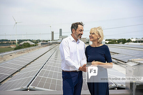 Happy businessman sharing mobile phone with businesswoman in front of solar panels on rooftop