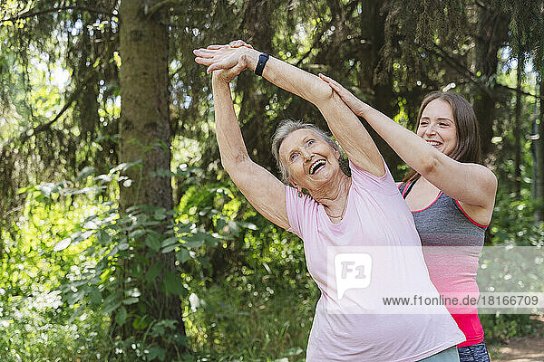 Happy fitness instructor guiding senior woman exercising in front of tree at park