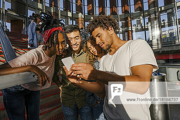 Young man sharing smart phone with multiracial friends at railroad station