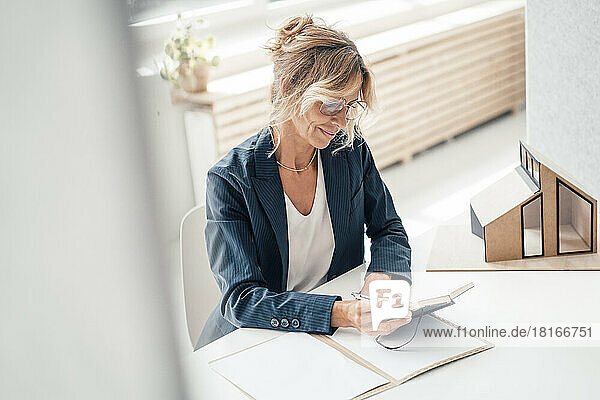 Smiling businesswoman looking at diary by house model on desk in office