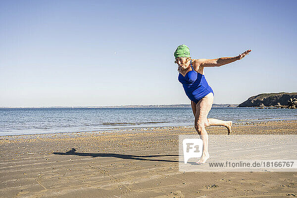 Senior woman running with arms outstretched at beach
