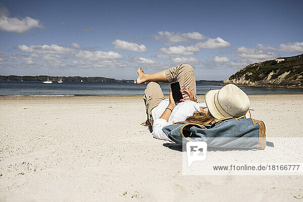 Woman with backpack using smart phone lying at beach